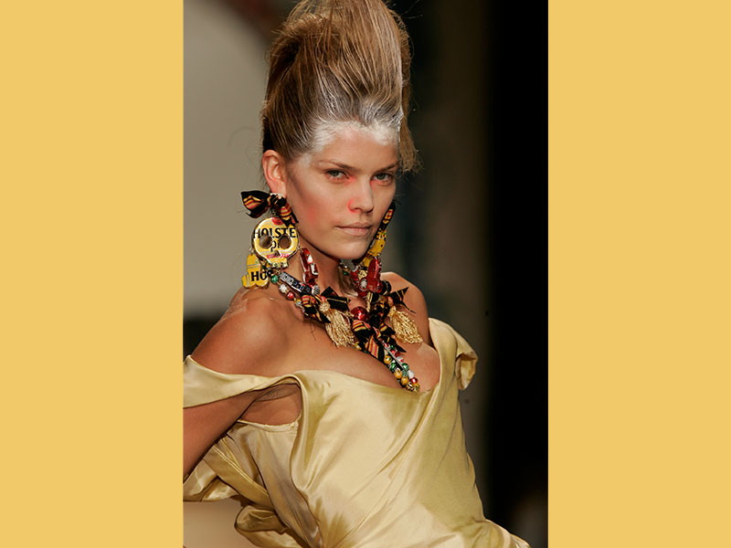 A model showcases a gold dress and unique costume jewelry made from recycled beer cans at a Vivienne Westwood show.