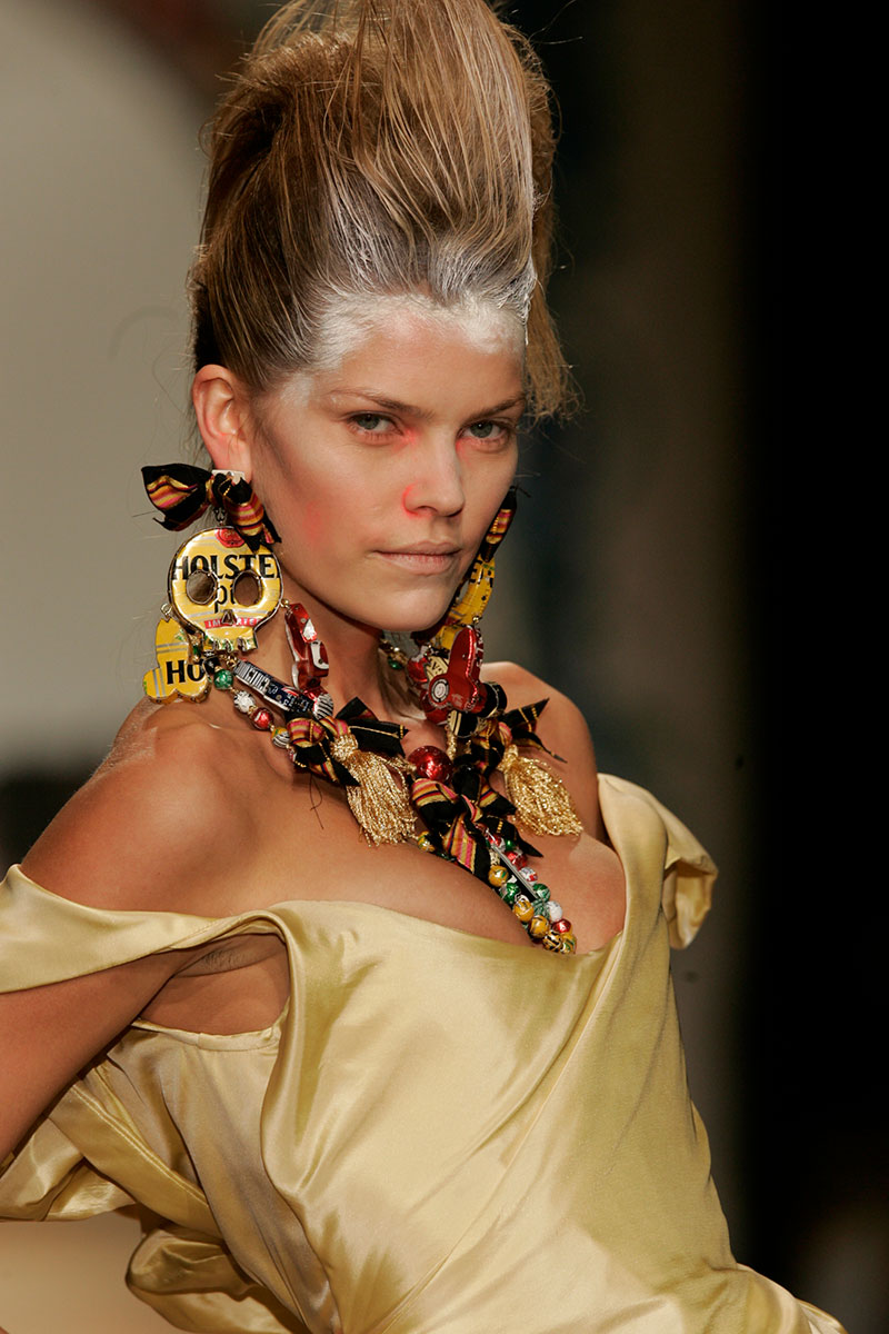 A model showcases a gold dress and unique costume jewelry made from recycled beer cans at a Vivienne Westwood show.