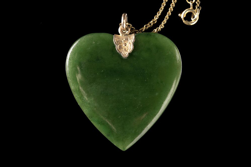 A piece of pounamu or greenstone carved in the shape of a heart, with a gold clasp and chain attached.