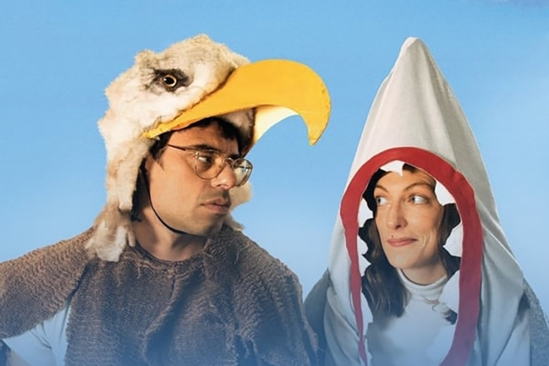 head and shoulders of two people looking at each other. The man has an eagle mask as a hat, and the woman is in a shark costume and is looking out through the teeth.