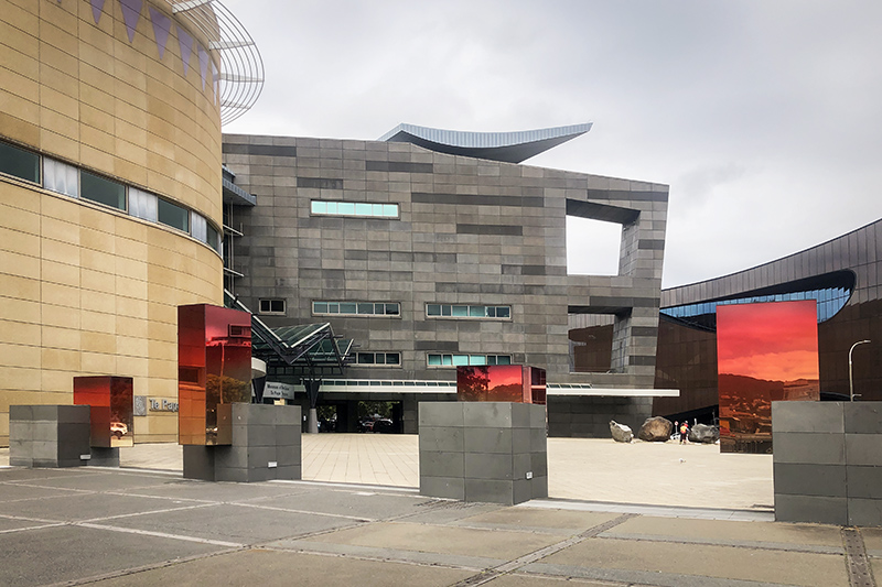 A phot of the forecourt of Te Papa with four concrete blocks lined up. Each of the blocks has a mirrored-glass rectangle at different positions on each.