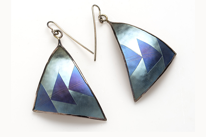 A pair of earrings on a white background. The earrings are large shell triangles with three more blue triangles inlaid in each.