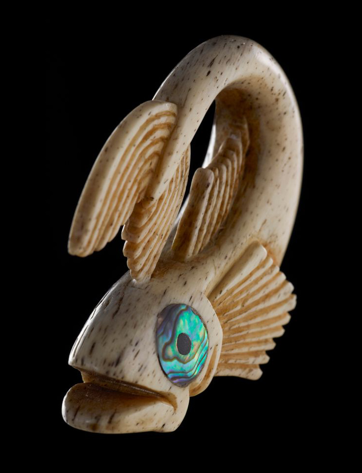 A stylised fish carved from bone with pāua shell eyes on a black background.