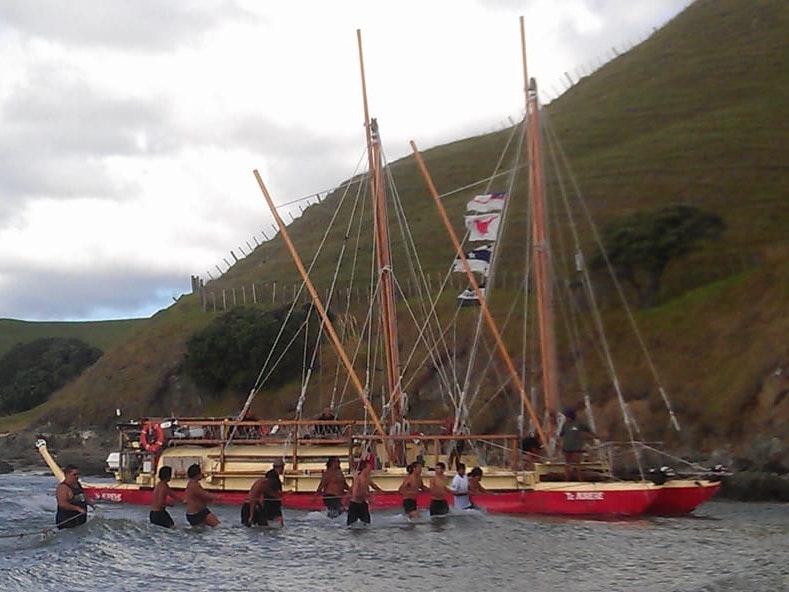 Crew members pull Te Aurere through Awapoko River near Aurere Beach after nine months of voyaging, 2013. Courtesy of Te Tai Tokerau Tarai Waka Inc and Jack Thatcher Men are standing in hip-high water and pulling a boat up a river.