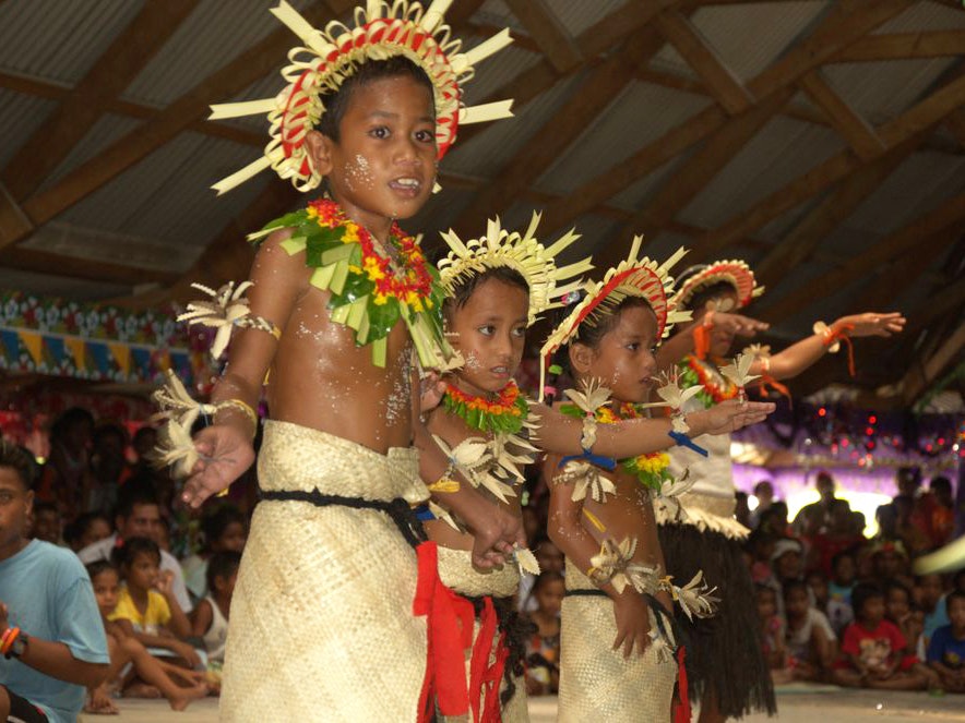 Mwaie Bikenibeu 2012 dance stills, Tony Whincup, Kiribati.  Gift of Tony Whincup estate, 2017. Te Papa (O.047354) Children in traditional Kiribati costume are performing for people.