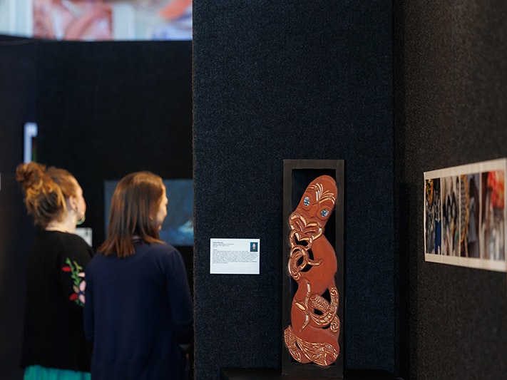 Mana Kōwhaiwhai: Our Visual Language, Te Wiki 2023. Photo by Jo Moore. Te Papa (235819) Two people are looking at artwork hung on a black wall.