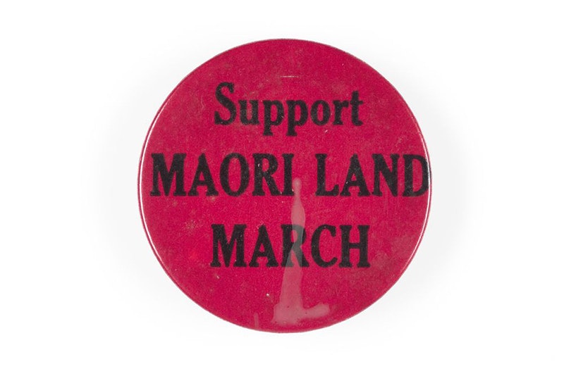 Support Maori Land March badge, maker unknown. Gift of Meg Bailey, 2020. Te Papa (GH025627) A dark pink badge with the words Support Māori Land March.
