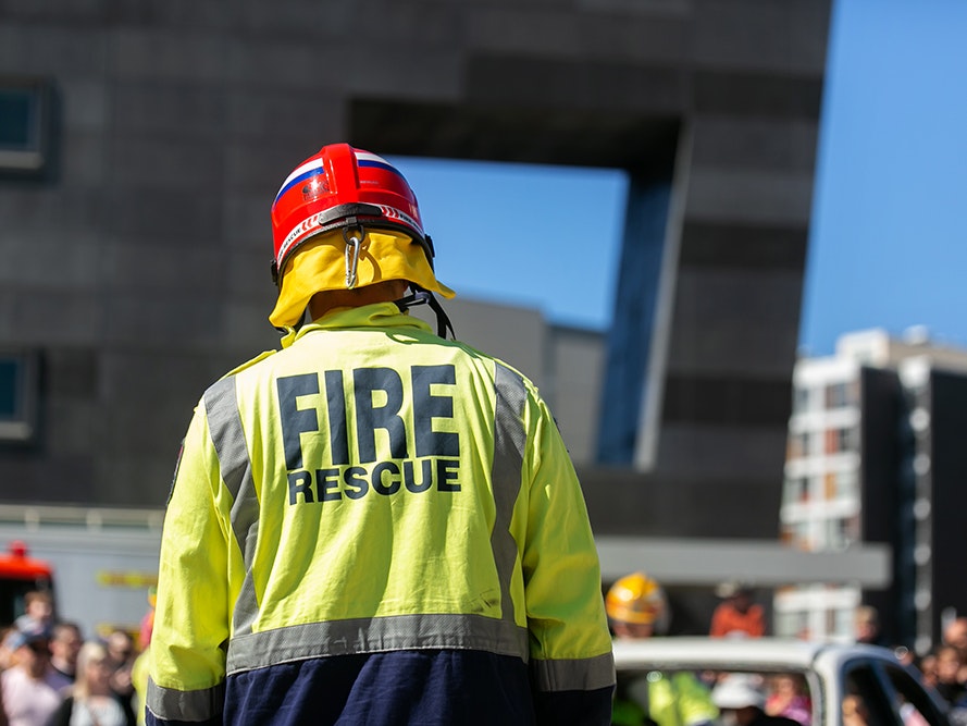 Emergency Services Expo, 2018. Photo by Jo Moore. Te Papa (116296) The back of a fire service person with a high-vis Fire rescue coat and hat on.