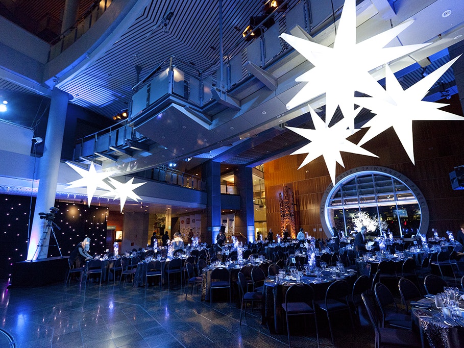 Matariki Gala 2012, photo by Kate Whitley. Te Papa (34414) A large gallery space at Te Papa set out with tables and chairs and giant white stars hanging from the roof.