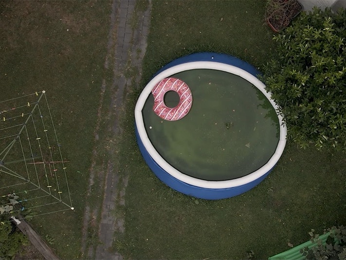 Still from Johanna Mechan video from Slow Burn, 2026 A top-down view of a back yard with a paddling pool and a rotary clothesline.