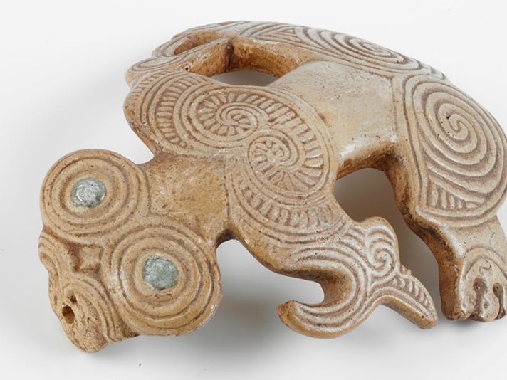 Skull tiki (plaster cast replica), D. Brucciani and Company; copyist; 1909; London. Purchased 1909. Te Papa (R000113) A small carving of a stylised figure with paua eyes sitting on a white surface.