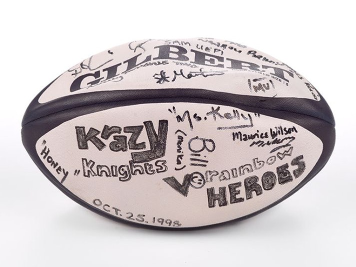 'Krazy Knights v Rainbow Heroes' rugby ball, 1998, India, by Gilbert Rugby. Gift of Alan Bracegirdle, 2020. Te Papa (GH025532) Ink signatures on a black and white, vinyl, 'Gilbert' brand rugby ball. Large block letters read "Krazy Knights v Rainbow Heroes" alongside a smiley face and the date "Oct.25.1998". Visible signatures include "Honey", "Ms. Kelly", "Bill (Monika)", Maurice Wilson" and " Mu".