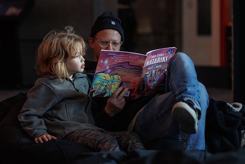Matariki Whānau Day 2025 Te Papa. Photo by Jo Moore. Te Papa (268687) An adult is reading a book about Matariki to a child.