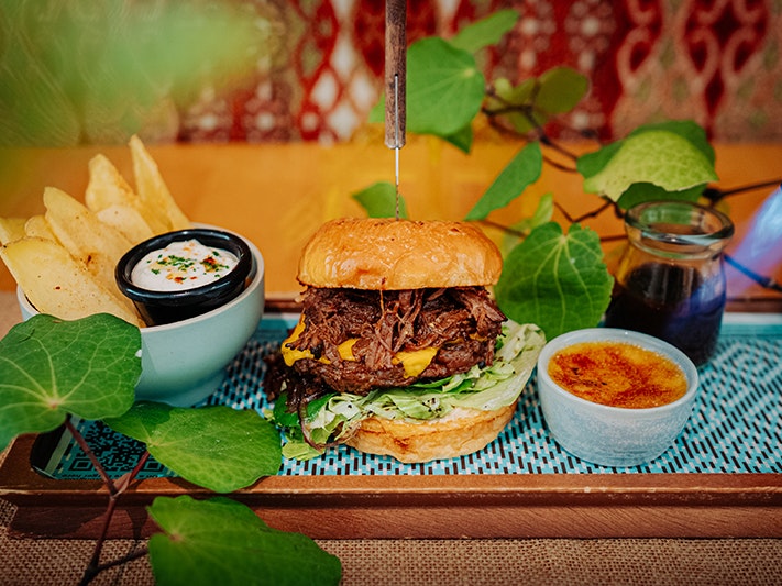 Wellington On a Plate at Te Papa Cafe, 2026. Photo by Beeline Creative. Te Papa (279610) A burger, frieds, a creme brulee dessert and some green leaves are displayed on a wooden tray.