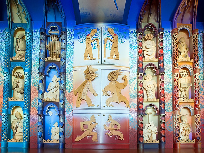 Detail of Te Hono ki Hawaiki, 2015. Photograph by Norm Heke. Te Papa (79630) Brightly carved figures made from MDF on a wall with six cupboards in a row with figures on them.