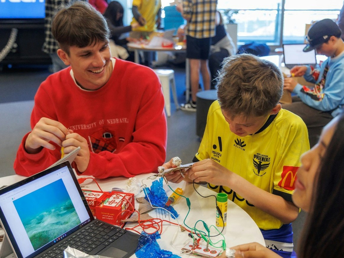 Students build their Kaitiaki Creator, 2025. Photo by Jo Moore. Te Papa A man and a child are working with a laptop and technology at a table.